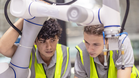 Vizualizácia praktického využitia Campus Networks v rámci vzdelávania, výskumu a testovacieho prostredia  – dvaja mladí výskumníci pozorujú robotické rameno v testovacom prostredí.