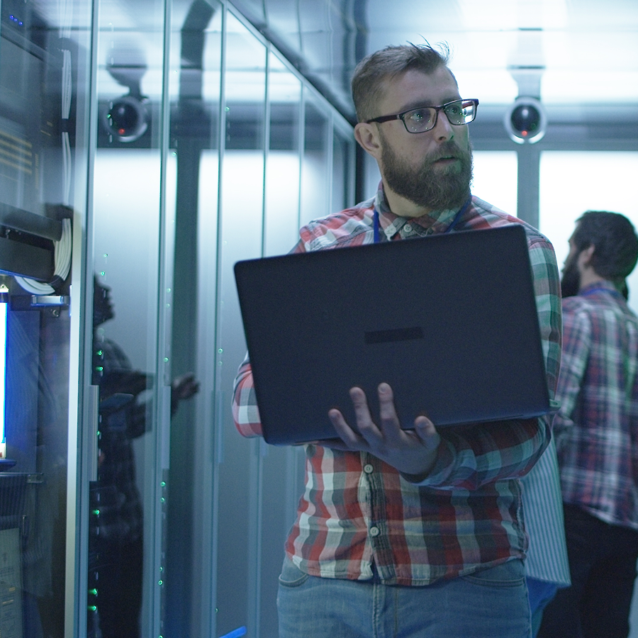 Muž v serverovej miestnosti drží notebook a vykonáva kontrolu serverov. Vizualizácia služby Telekom Cloud Server pre stredné a veľké firmy.