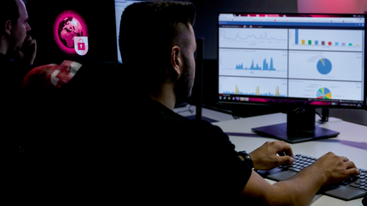 Analytik sleduje grafy a štatistiky na monitore v tmavej miestnosti. Vizualizácia témy digitálnej bezpečnosti a zachytávania kybernetických hrozieb so službou Security Scan.