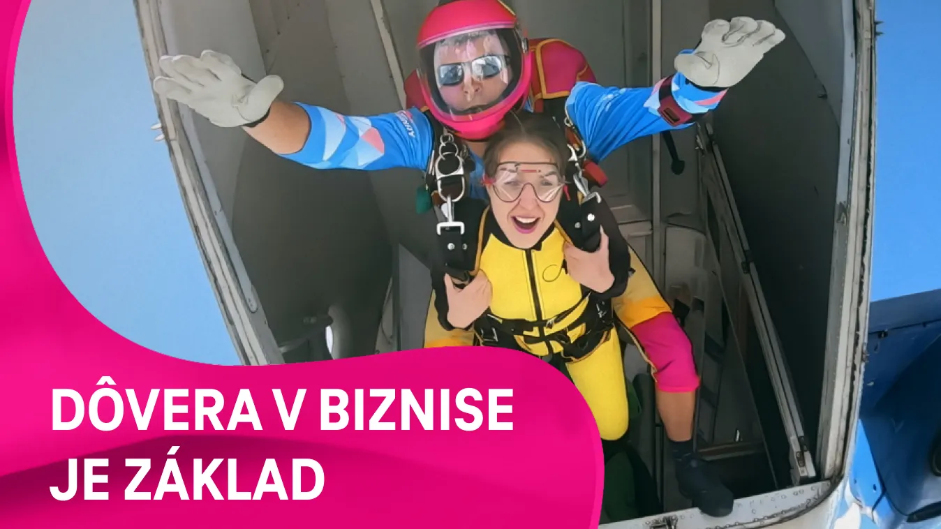 tandemový zoskok – inštruktor s prilbou a okuliarmi stojí s pripútanou ženou v otvorených dverách lietadla pred skokom