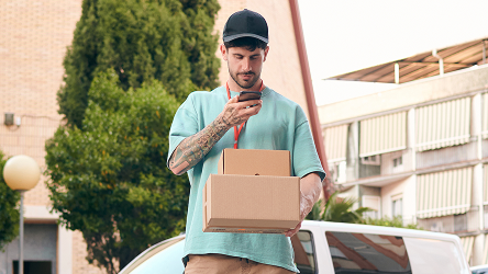 Kuriér kontroluje telefón pri doručovaní balíka – ilustruje spoľahlivé pripojenie a zvládnutie objednávok v teréne.