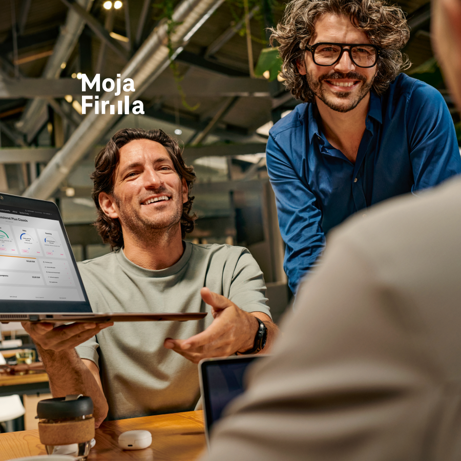 Dvaja muži sa usmievajú počas pracovného stretnutia a jeden z nich ukazuje na notebook s prehľadom firemných služieb od Slovak Telekomu. Vizualizácia digitálnej správy telekomunikačných služieb cez portál Moja Firma.