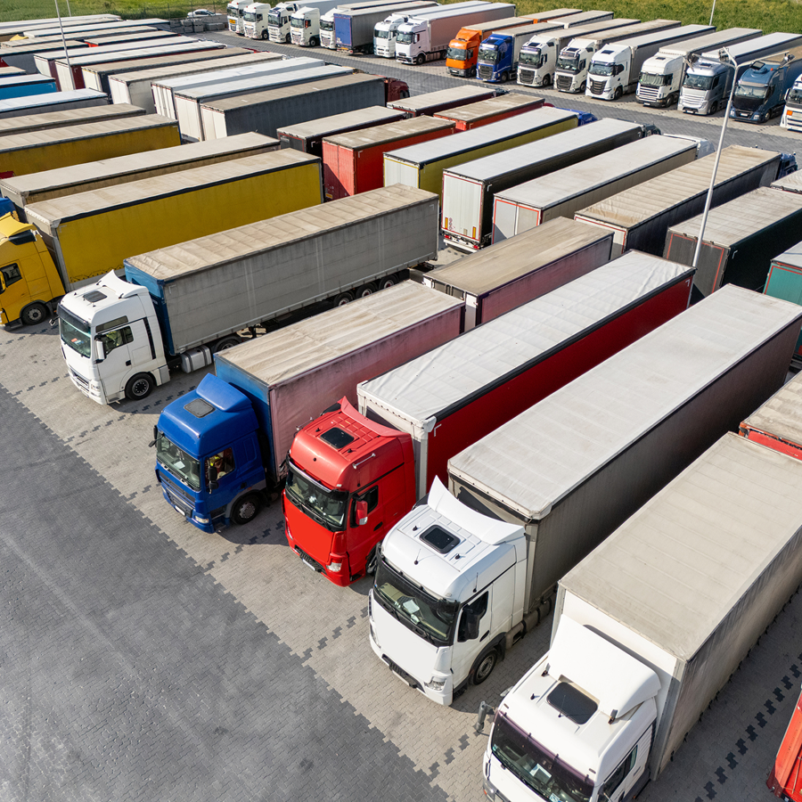 Rôznofarebné nákladné vozidlá zaparkované v rade na firemnom parkovisku – vizuál služby Monitoring vozidiel od Telekomu.