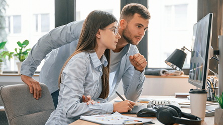Dvaja kolegovia v marketingu intenzívne spolupracujú nad návrhom na veľkom monitore – reprezentuje prácu v reálnom čase cez cloudové služby.