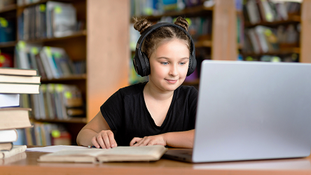 Študentka v knižnici používa notebook a slúchadlá – vizualizuje bezpečný prístup k internetu a kontrolu obsahu v školskom prostredí.