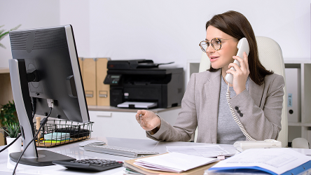 Administratívna pracovníčka telefonuje pri stole s počítačom v kancelárii.