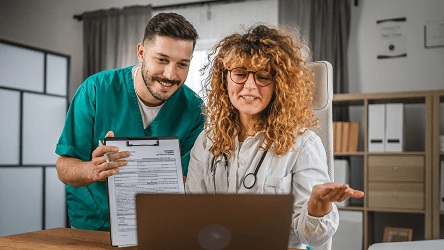 Zdravotnícky personál konzultujúci údaje pri počítači – vizuál služby Telekom SMS & RCS Messaging.