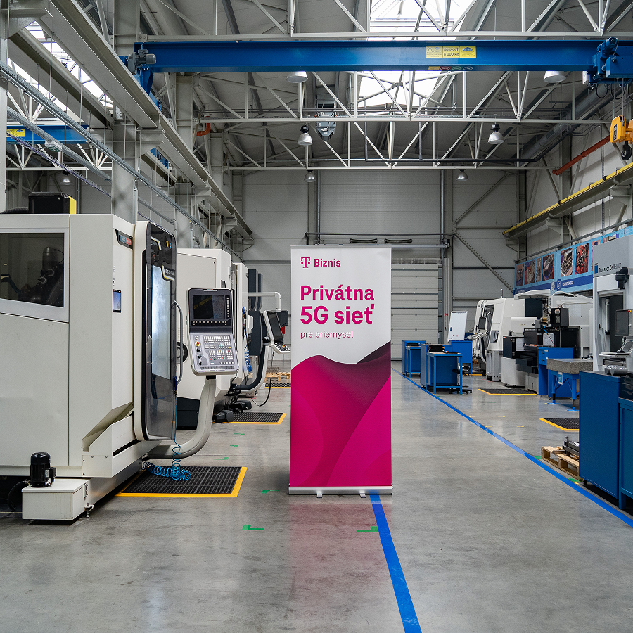 Výrobná hala s modernými strojmi a rollupom s nápisom „Privátna 5G sieť pre priemysel“. Vizualizácia spolupráce Telekomu s vysokými školami pre zavádzanie technologických inovácií do praxe.